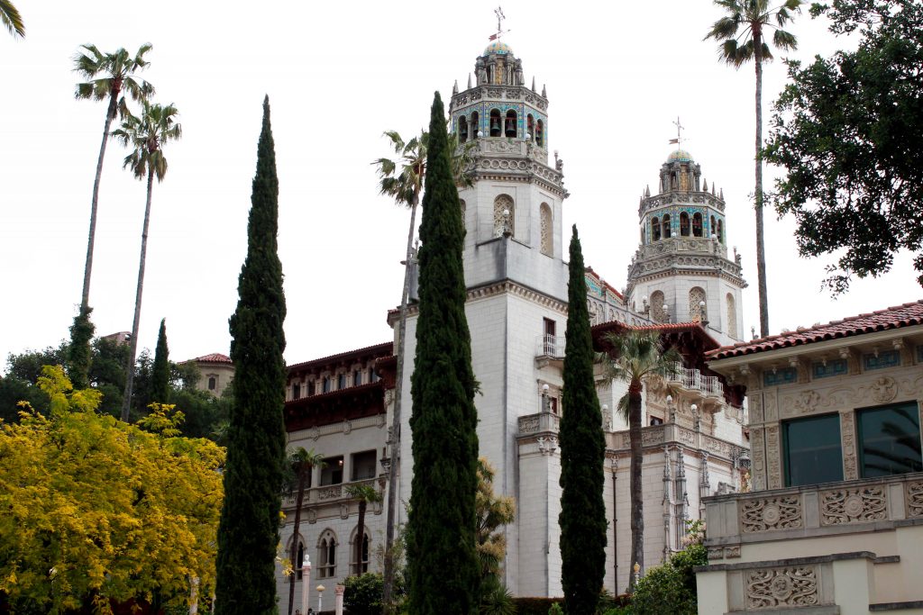 a side view of hearst castle with cypress tress in the foreground