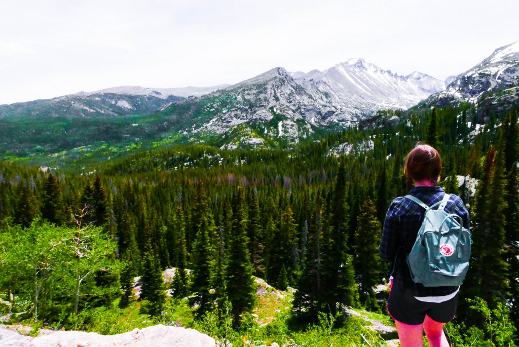 A girl with a blue backpack staring out at the Rocky mountains - the perfect day trip for a Denver itinerary