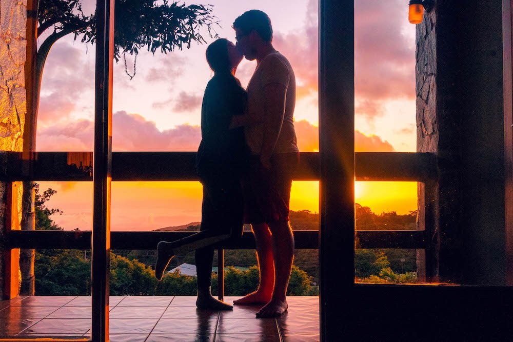 Addie and Daniel kissing on a balcony in front of the sunset in Monteverde
