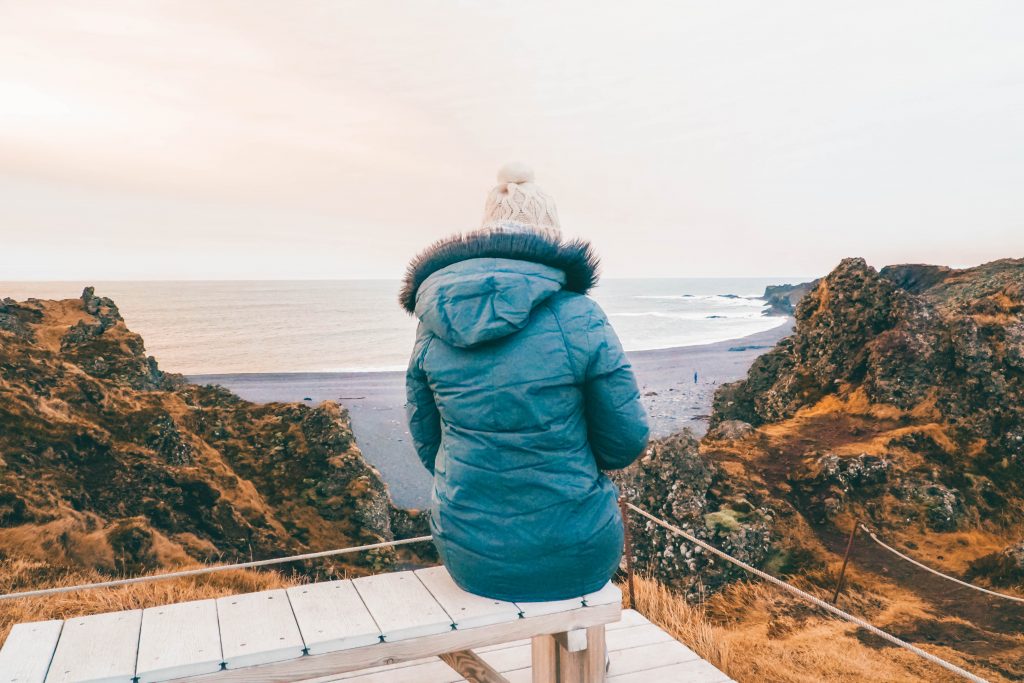 Addie sitting on a bench staring at a black sand beach in Iceland in december