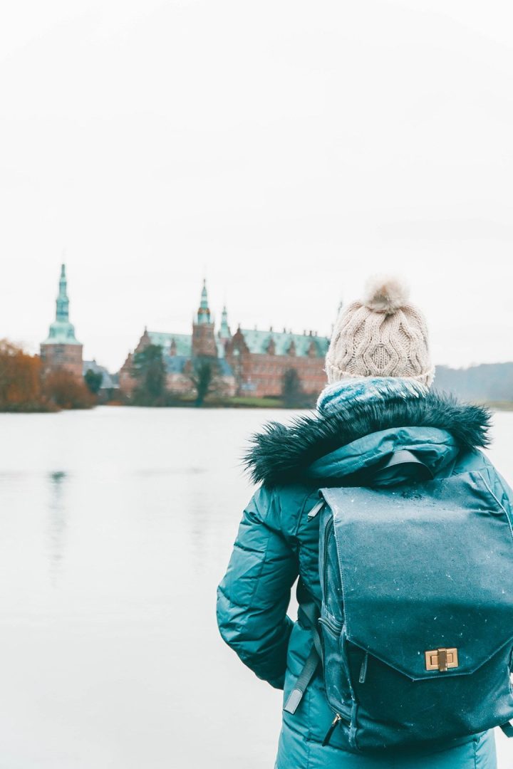 Addie staring across the way at Frederiksbog Castle in Denmark with a camera backpack - travel photography essentials