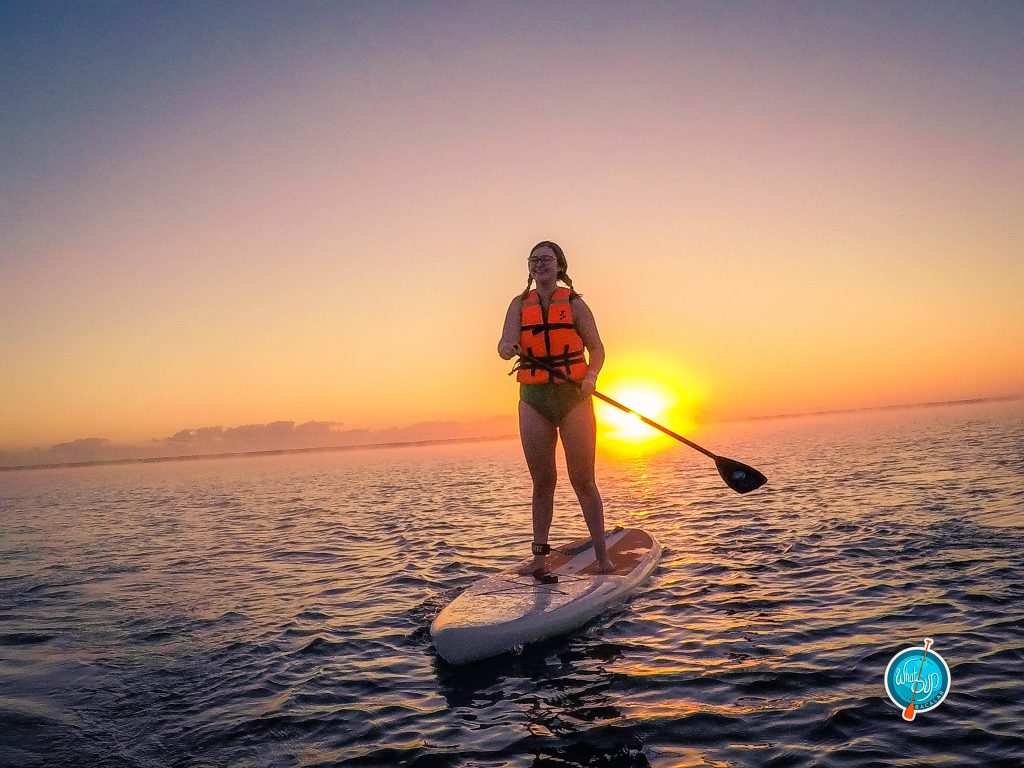 Addie smiling big while standing on a paddlebord during sunrise in Bacalar, Mexico