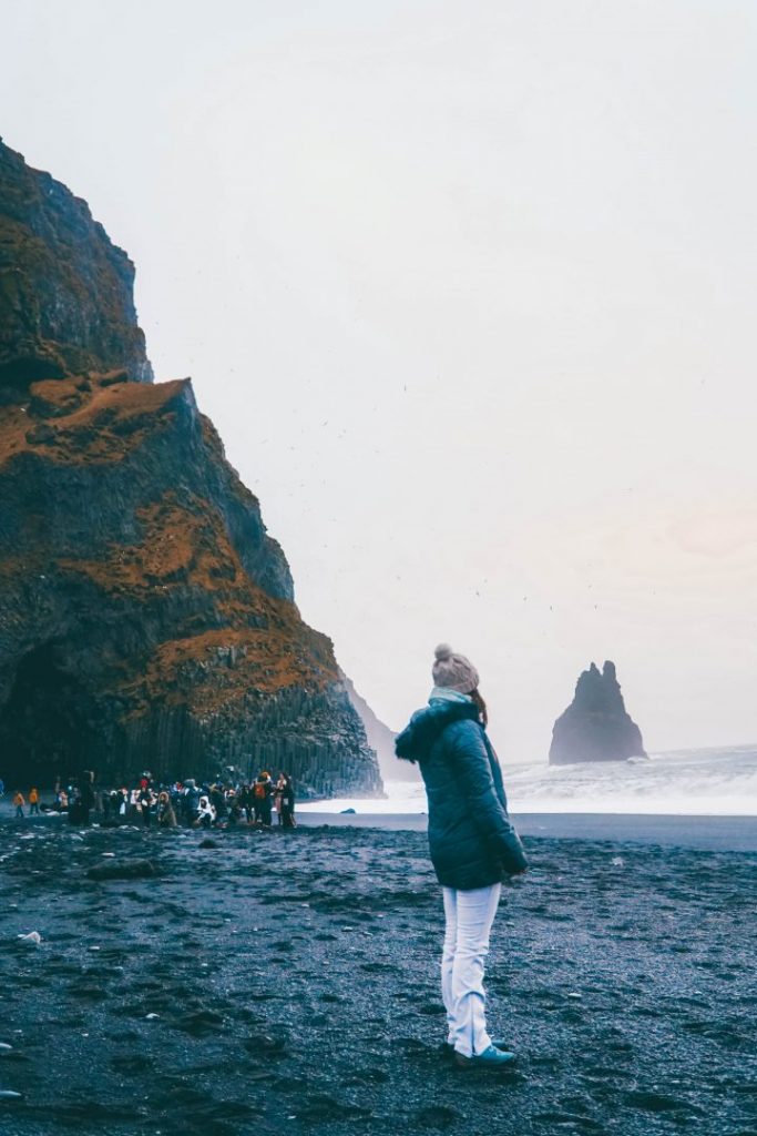 Addie standing on a black sand beach in Iceland, a crowd in the background