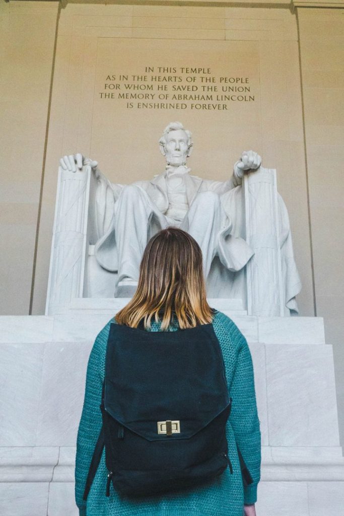 Addie in a green sweater and black backpack staring up at the statue of Abraham Lincoln in the Lincoln Memorial in Washington DC