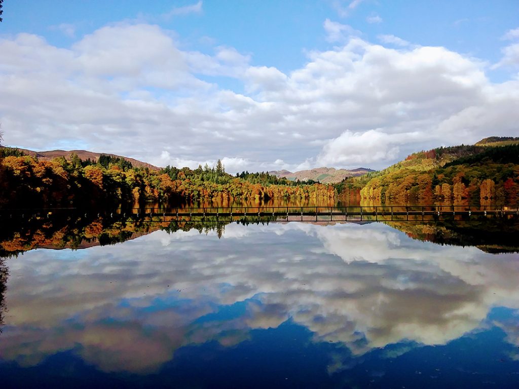 A lake reflecting the clouds and autumn color trees in Perthshire, Scotland