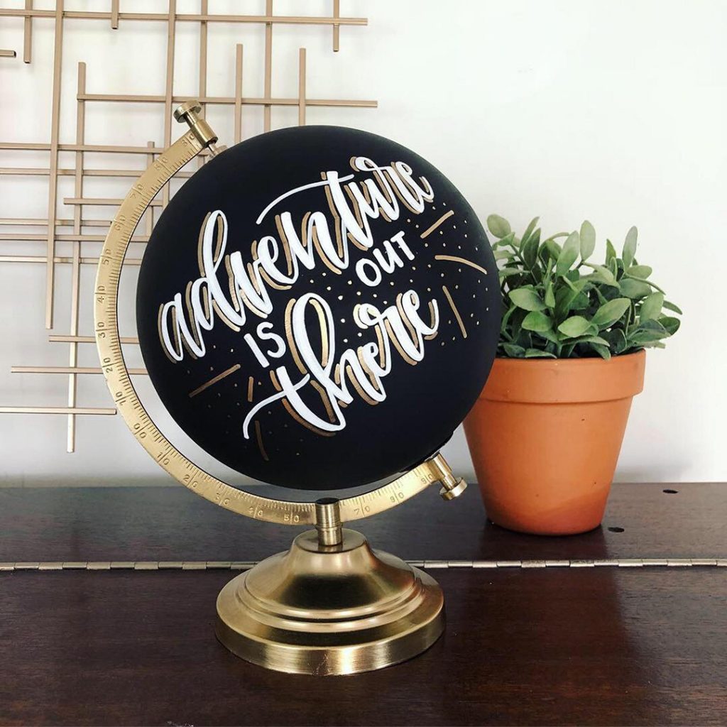 A black painted globe that says "Adventure is out there" - one of the best travel gifts for her