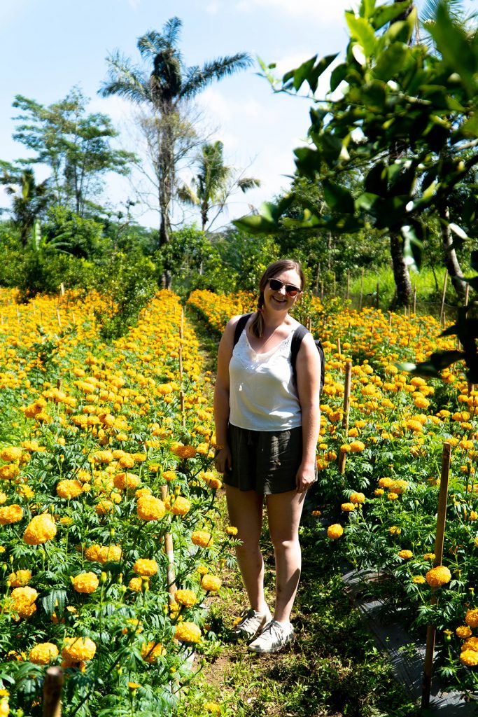 Addie standing in field of magnolias on a bike tour in Bali. Experiencing your destination more deeply is one of the top reasons to travel solo.