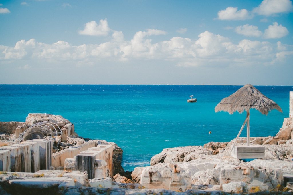 ruins and a small straw umbrella by the ocean in Cozumel, mexico