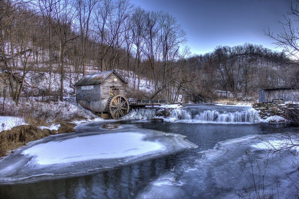 a small brown cabin with water wheel on a frozen over river in Wisconsin