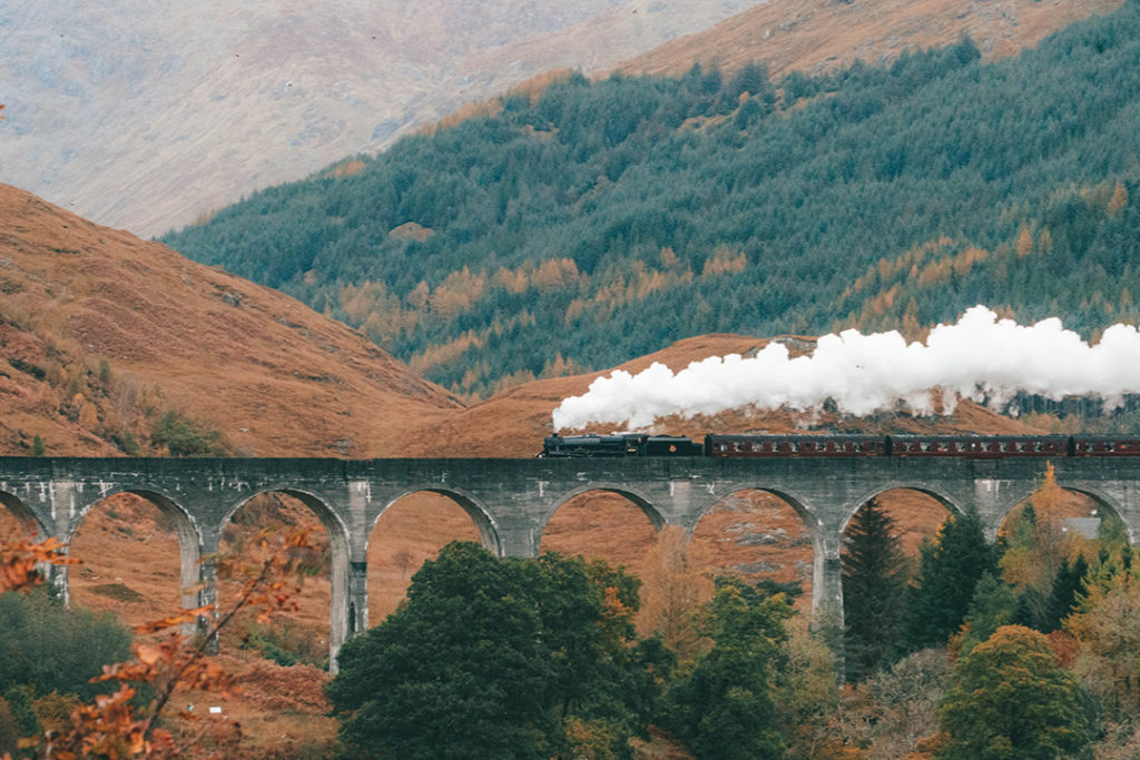 the jacobite steam train going over the glenfinnan viaduct with lots of steam