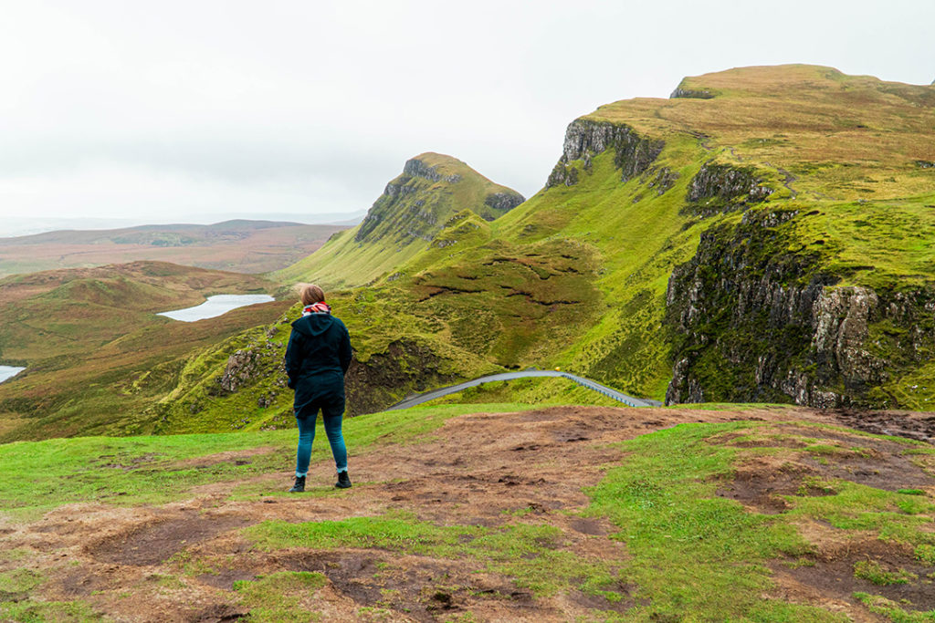 addie standing in front of the rolling hills of the quiraing on the isle of skye, one of the best solo female travel destinations!