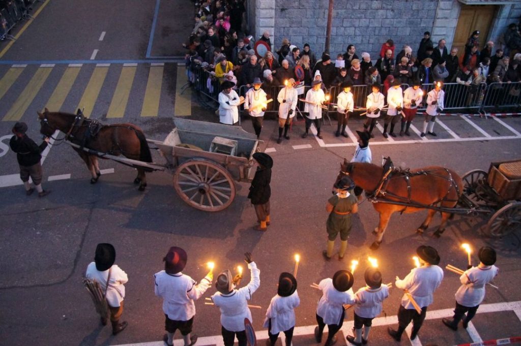 people in old-fashioned costumes holding candles as horses pulling carts go through the street in Geneva, one of the best places to visit in Europe in winter