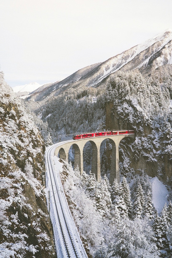 a train going over a viaduct in a snowy mountain landscape