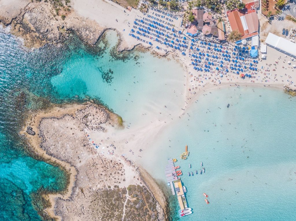 a photo from the air of vivid blue water and umbrellas on a beach in Cyprus