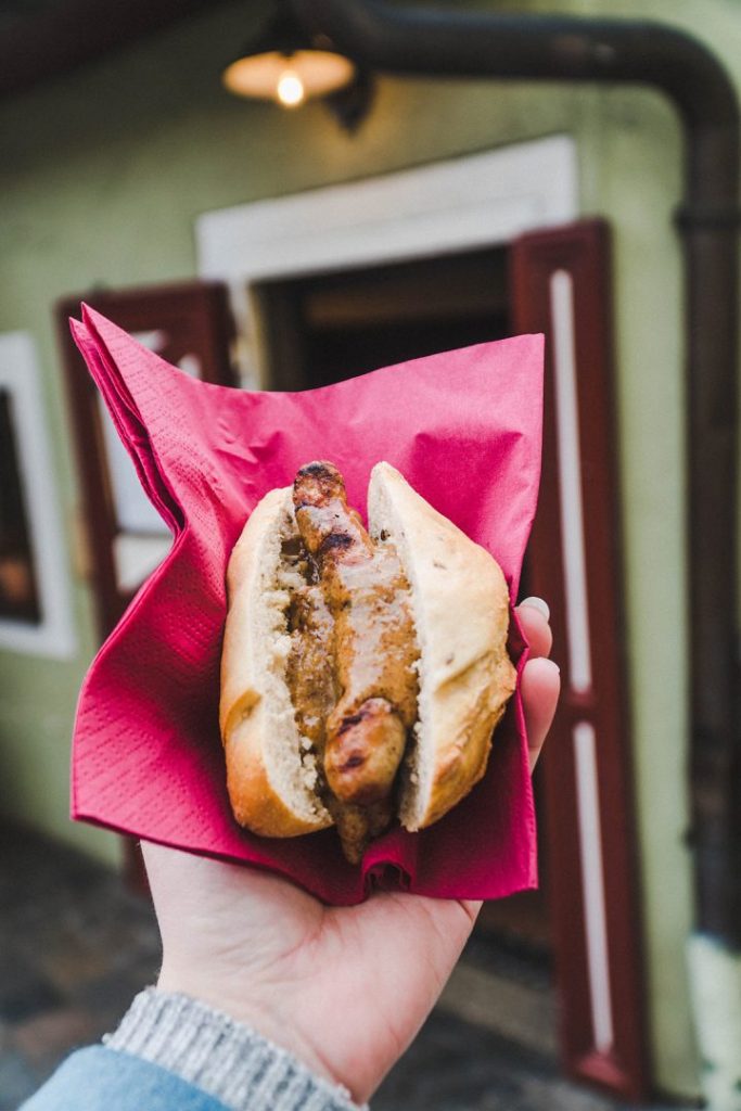 a hand holding up a bread roll filled with three small sausages