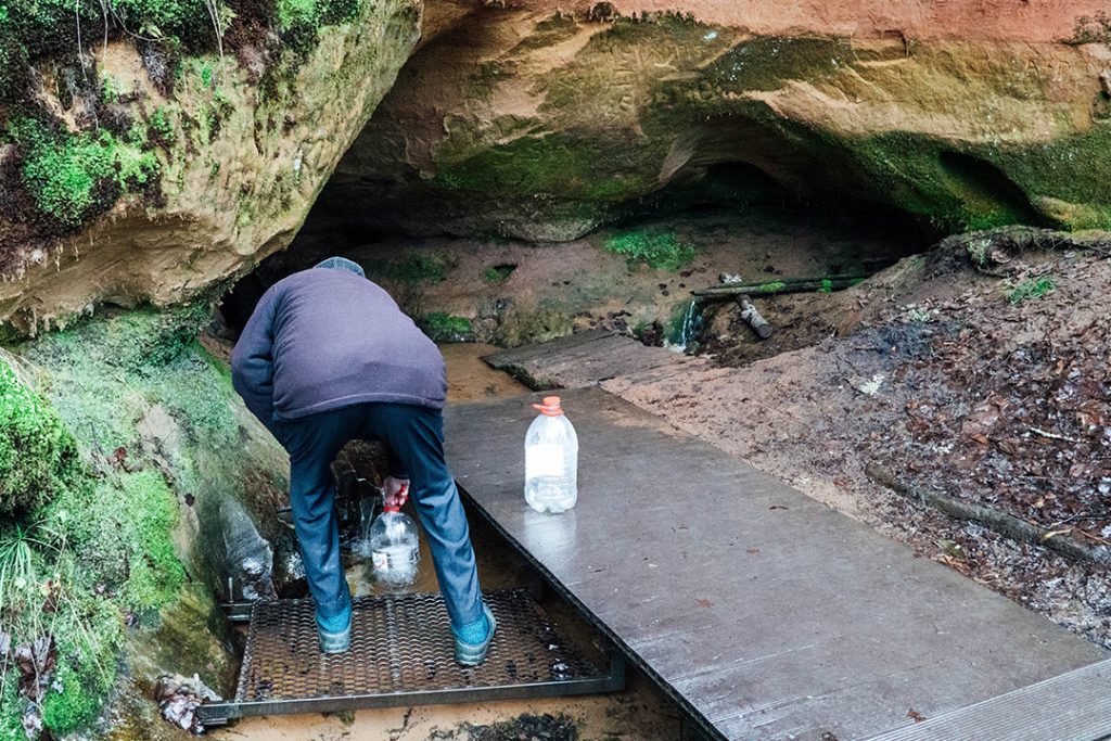 a man filling up a large water bottle from a fresh spring