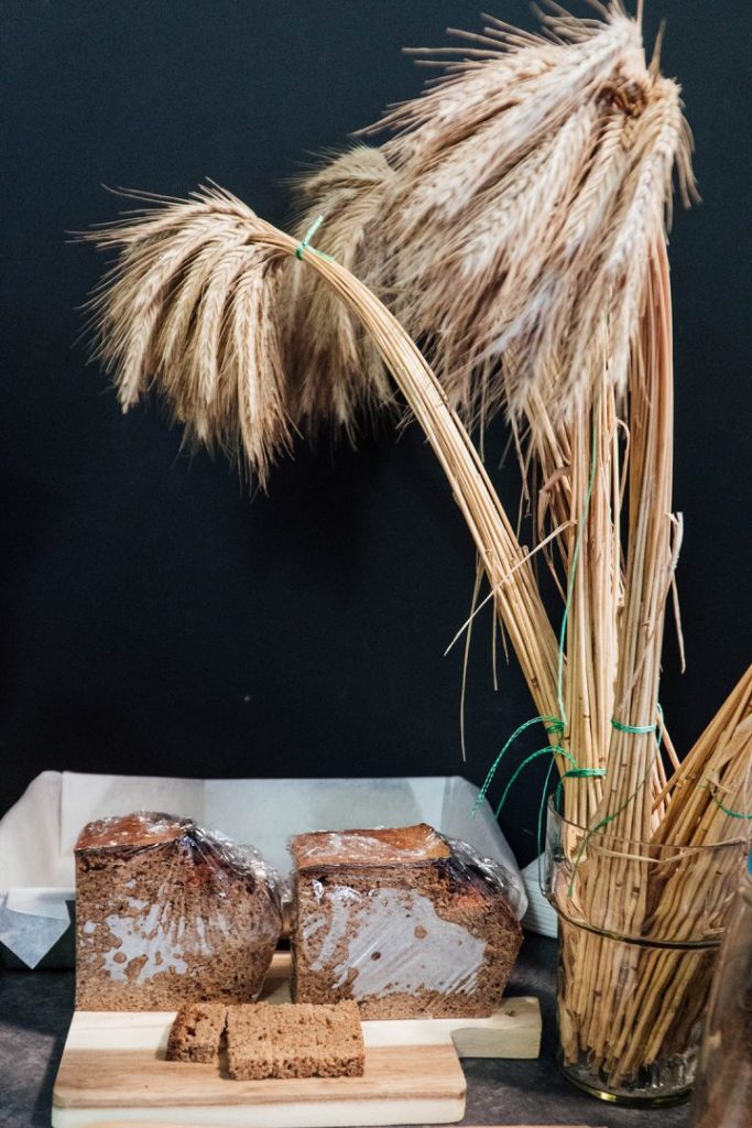 bread on a cutting board and wheat stalks in a vase