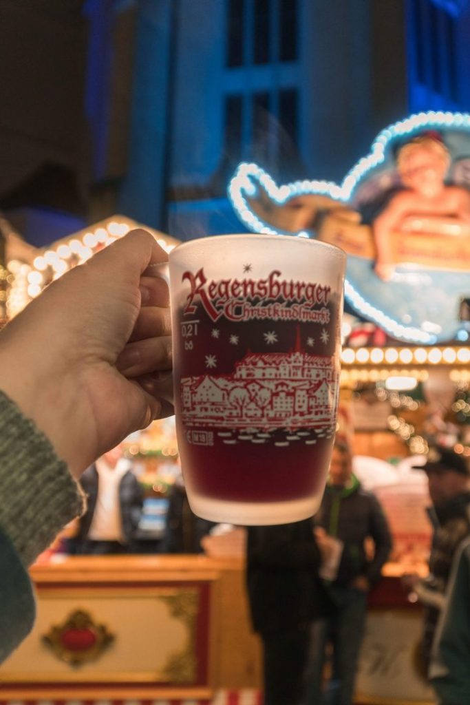 A hand holding up the Regensburg Christmas Market gluhwein mug, filled with red gluhwein