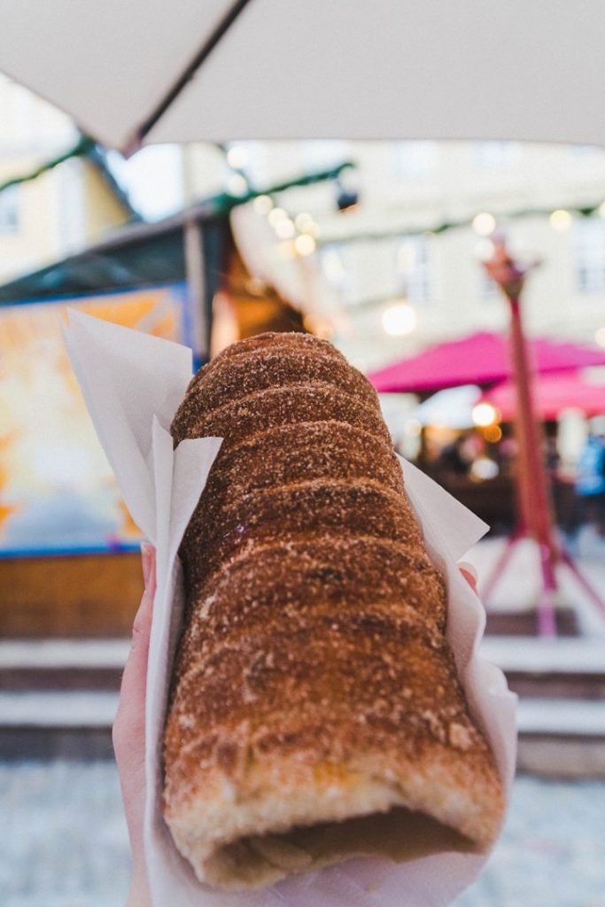 a hand holding up a chimney cake - dough rolled up in a spiral