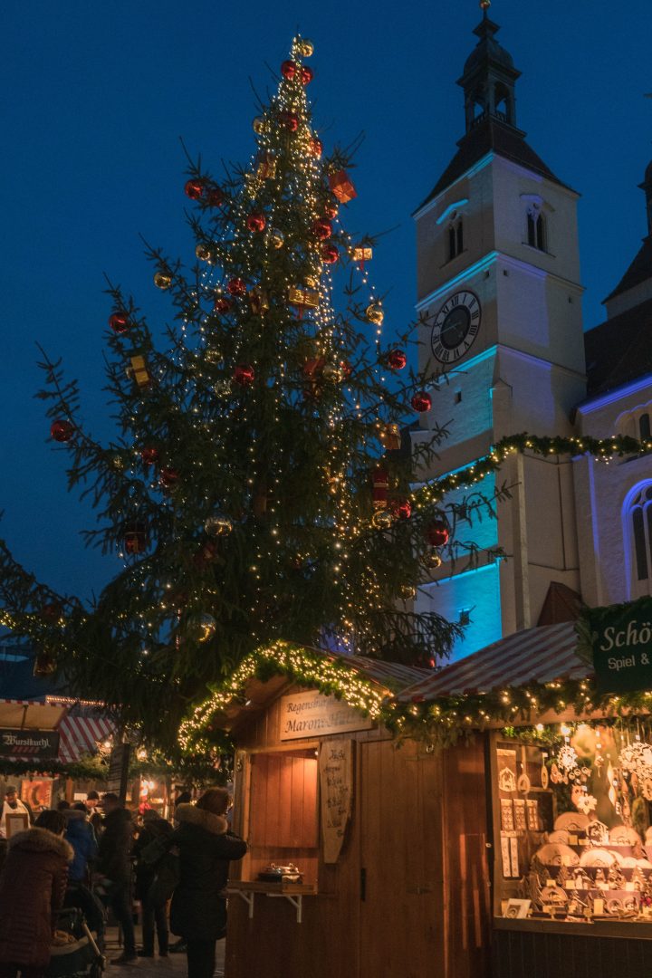 small wooden booths and a large christmas tree lit up at night