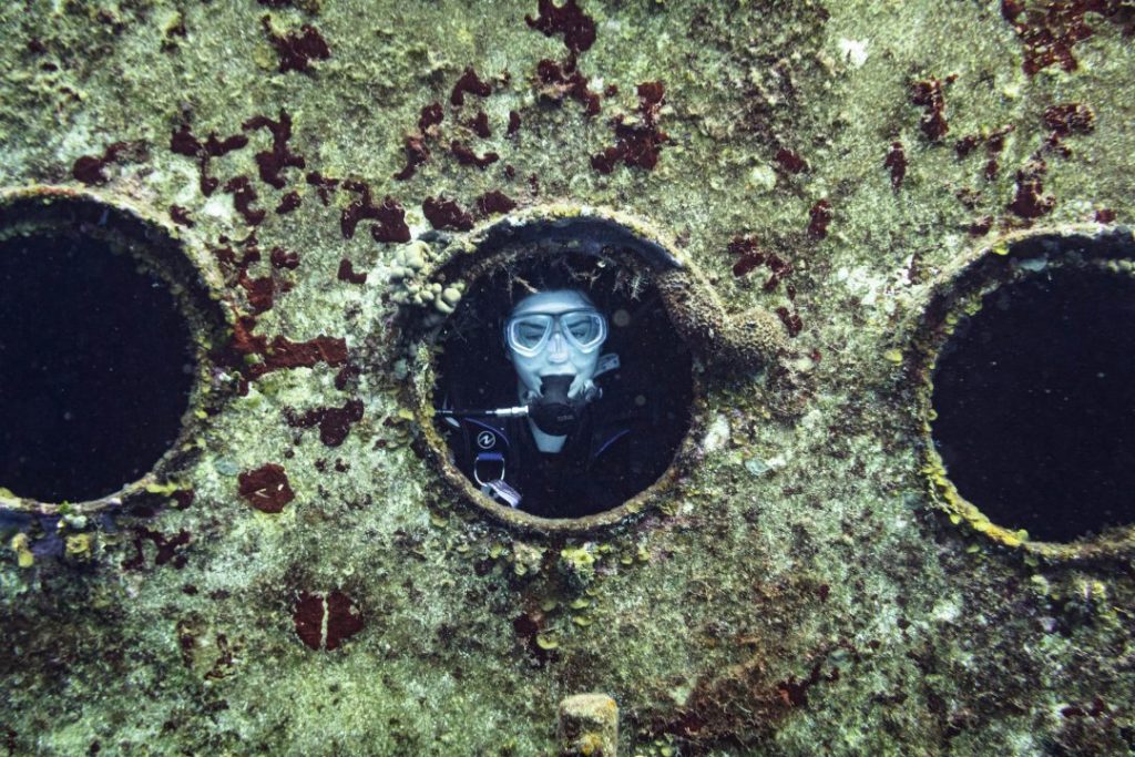 addie in full scuba gear peeking through the porthole of a shipwreck - cozumel scuba diving