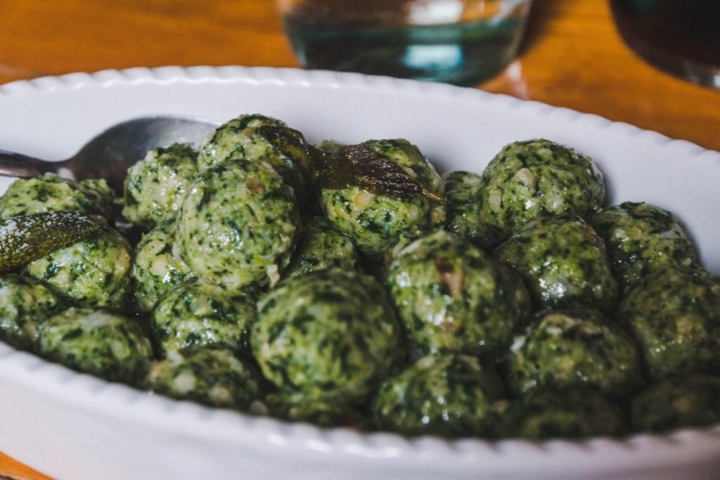 Green strangolapreti dumplings piled high in a white dish, a specialty in in Valle di Ledro, Italy