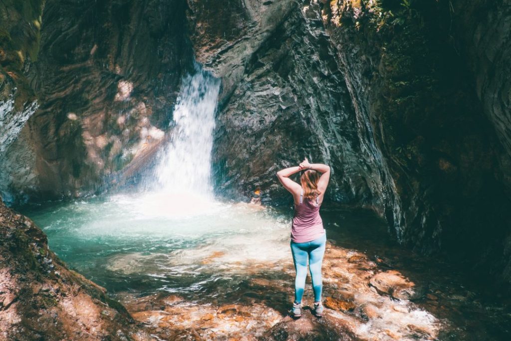 Addie standing proudly with her hands on her head in front of a waterfall - freedom is one of the best reasons to travel solo