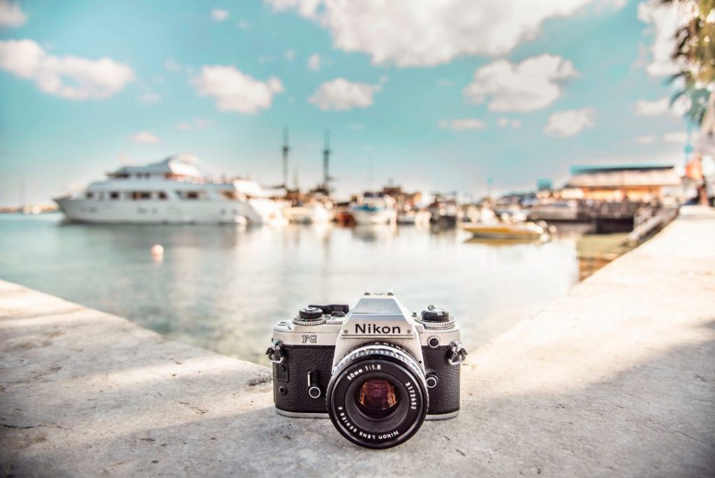 A Nikon camera sitting on the sidewalk by a harbor full of boats