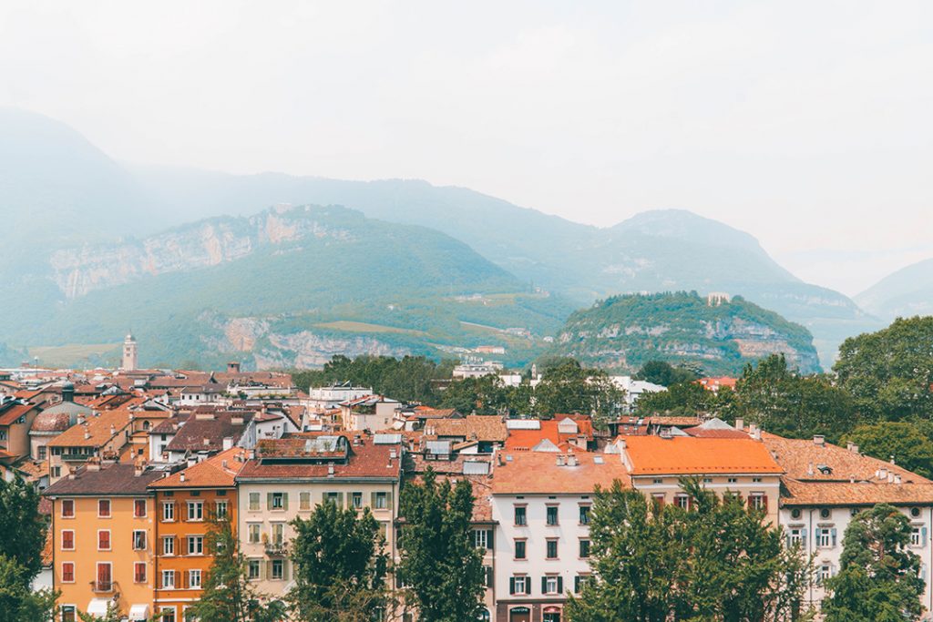 mountains in the background of a town with red roofs. Trento is one place to visit in Trentino