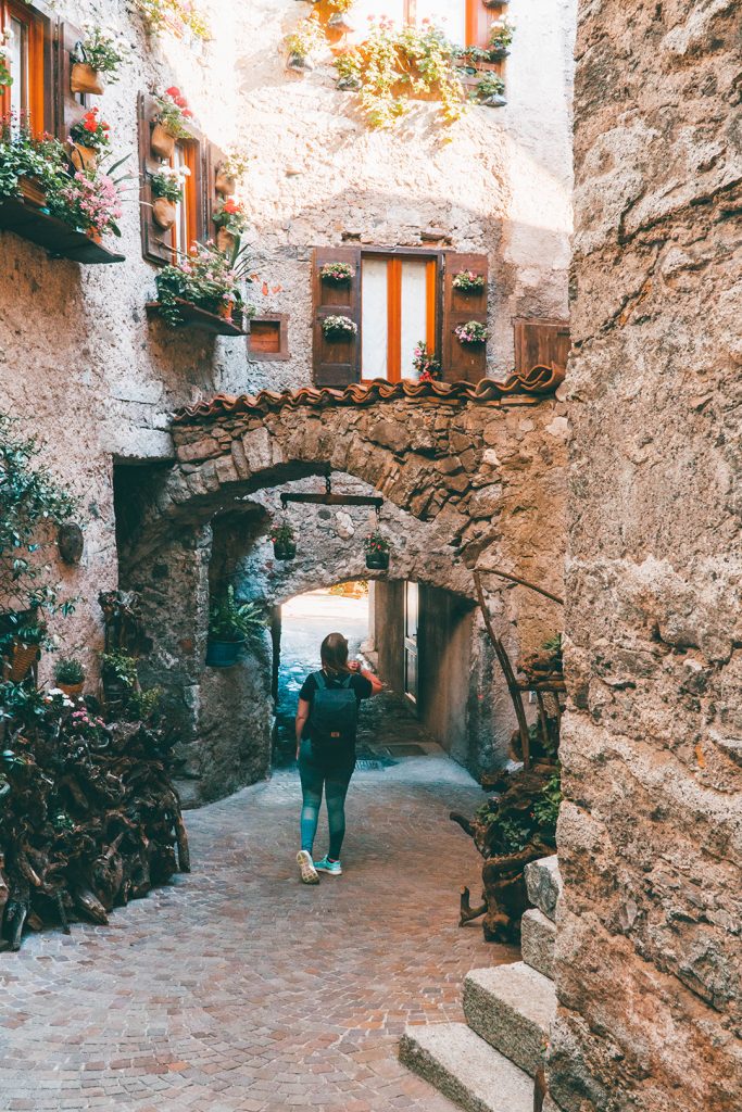 addie walking through a stone arch in baitoni, italy - one of the best places to visit in trentino!