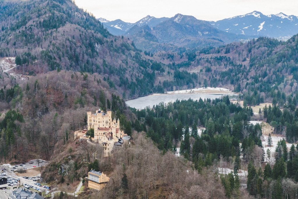 hohenschwangau castle perched on a hill with mountains and a lake in the background