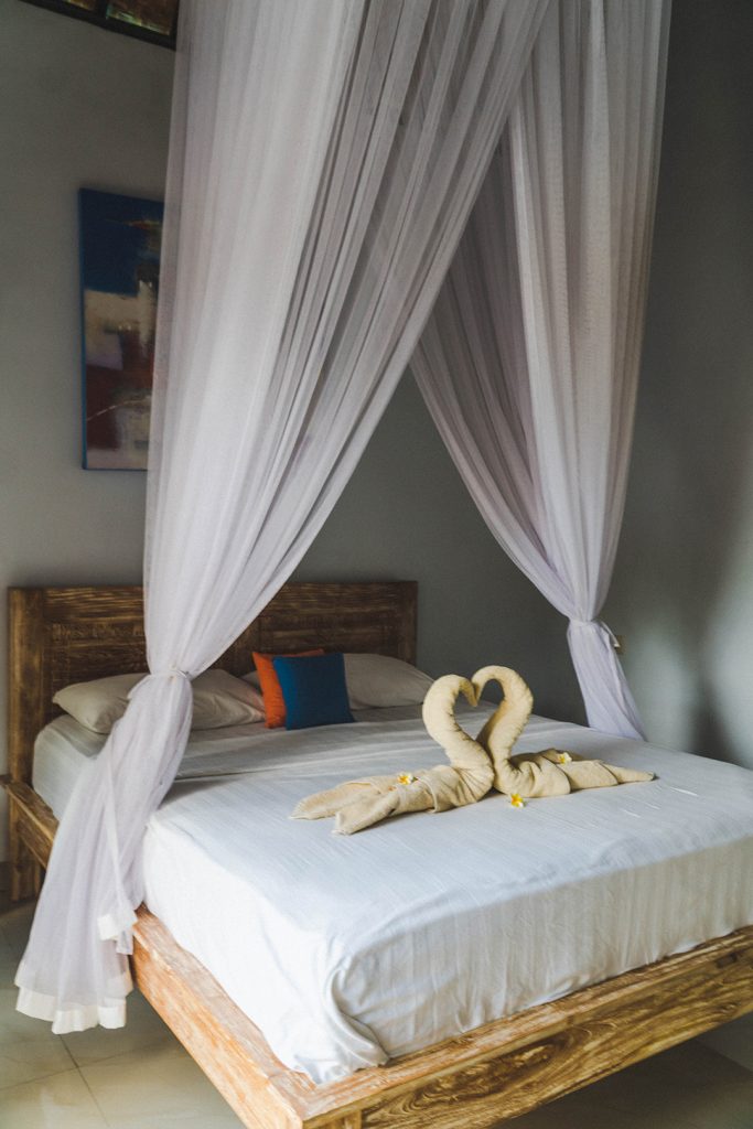 a bed with a mosquito net and two towel swans at Krisna Guest House - nusa islands guide