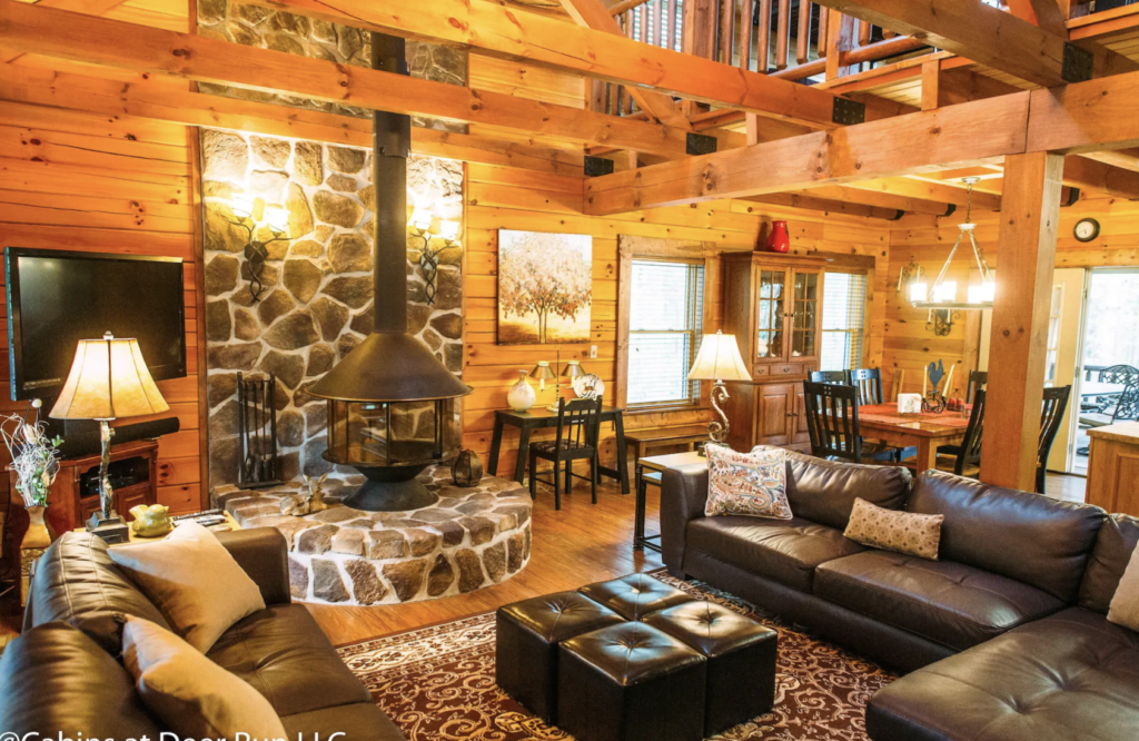a living room with a stone fireplace, leather couches, and exposed wood beams