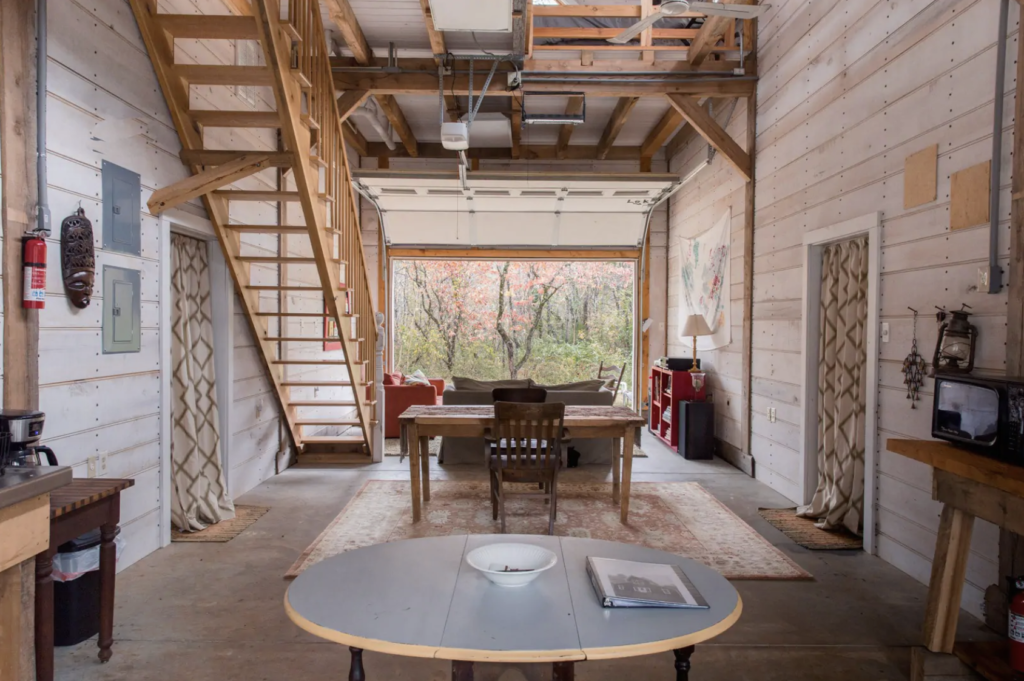downstairs in the remodeled barn, with a dining room set and wooden stairs leading upstairs