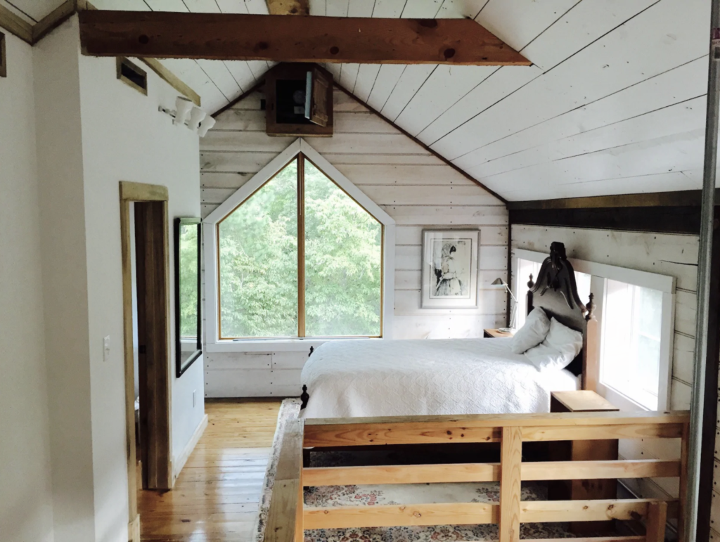 a comfortable looking bed in the loft of a remodeled vintage barn